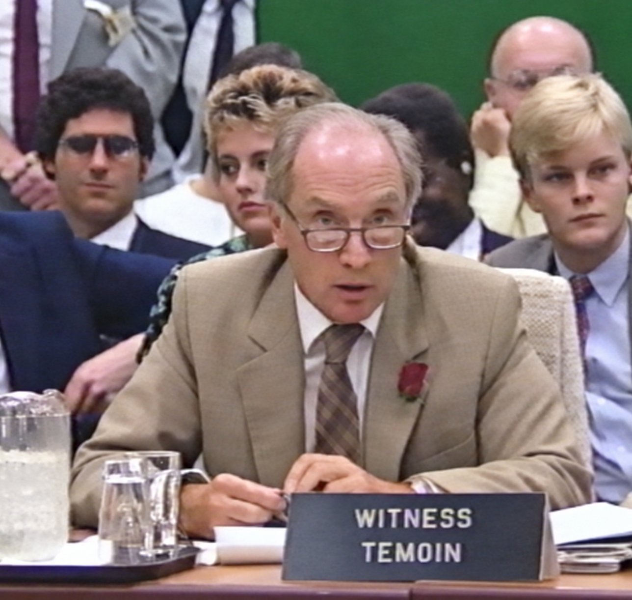 Pierre Elliott Trudeau speaking at the witness table, a WITNESS / TÉMOIN name card before him, with spectators seated behind